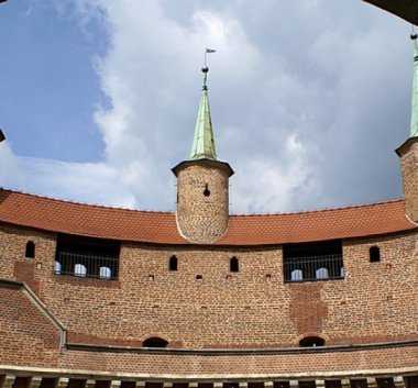 Kolorowa fotografia. Budynek Barbakanu z widocznymi murami i wieżyczkami.