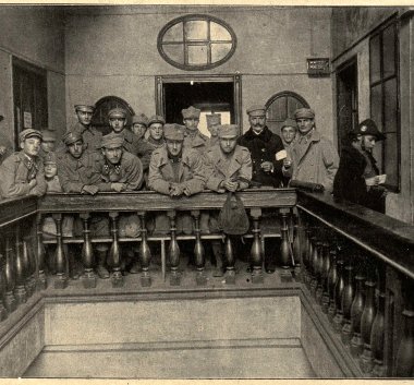 Zdjęcie w sepii.  Mężczyźni w wojskowych mundurach stojący przy balustradzie w budynku.