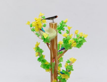 Fotografia drzewka emausowego. Zielono żółte drzewko z ptaszkiem na górze pnia.