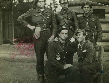 Fotografia czarnobiała. 5 mężczyzn ubranych w niejednolite mundury pozujących do pamiątkowego zdjęcia.]