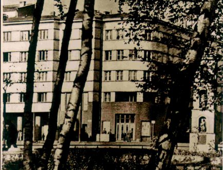 Fotografia czarnobiała. Budynek od strony Parku Krakowskiego w ujęciu między drzewami