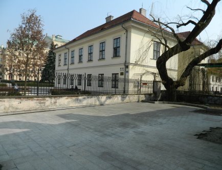 Kolorowa fotografia przedstawiająca budynek Domu Pod Krzyżem wraz z najbliższym otoczeniem.