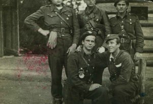 Fotografia czarnobiała. 5 mężczyzn ubranych w niejednolite mundury pozujących do pamiątkowego zdjęcia.