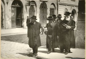 Fotografia czarnobiała. 6 idących mężczyzn, w tym dwóch w futrzanych czapkach na głowie.