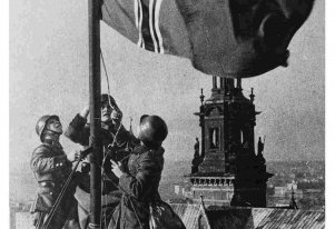 Fotografia czarnobiała. Trzech żołnierzy niemieckich, na dachu wciąga flagę na maszt. W tle wieża Katery Wawelskiej