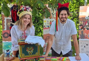 Fotografia. Kobieta w koronie i mężczyzna w czapce krakowskiej. Na stole tradycyjna skrzynia.