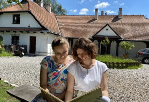 Kolorowa fotografia przedstawiająca dwie osoby czytające książkę. W tle budynek Rydlówki, oddziału Muzeum Krakowa.