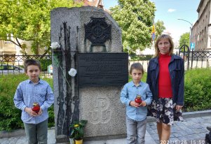 Kolorowa fotografia. Kobieta i dwójka dzieci stojąca przy pomniku