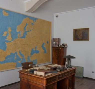 Kolorowa fotografia. Biurko z dokumentami. Na ścianie mapa Europy.