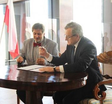Zdjęcie przedstawiające dwóch mężczyzn siedzących przy biurku i podpisujących umowę